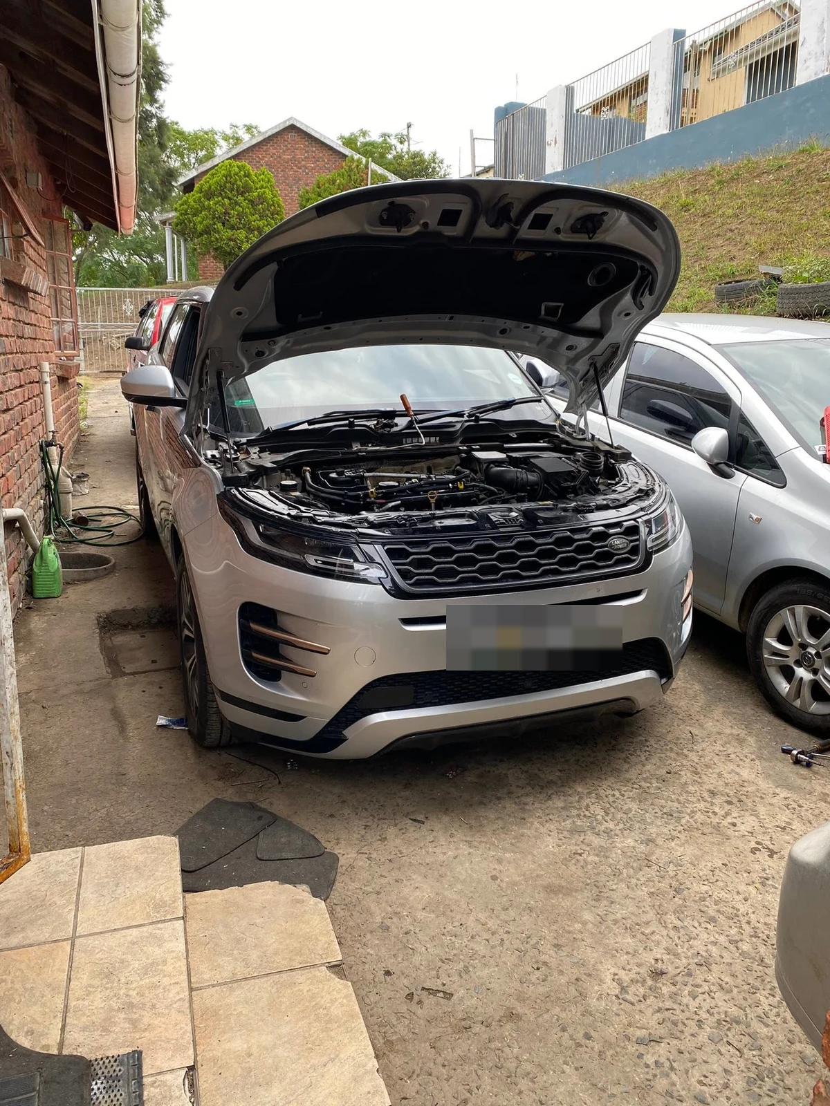 A silver SUV parked outdoors in daylight with its bonnet raised, number plate redacted